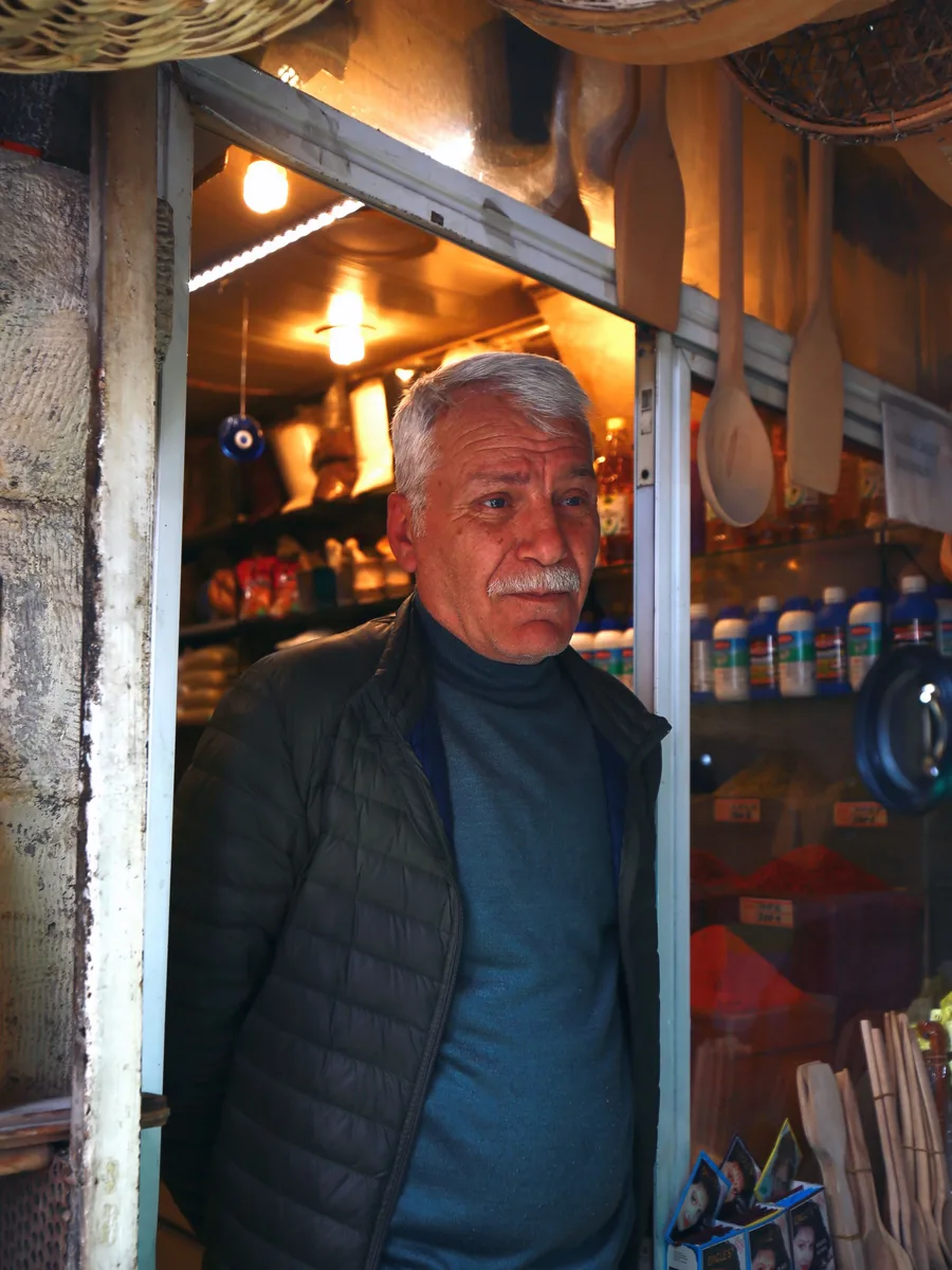 A shopkeeper standing in the doorway of his shop, shelves of goods behind him